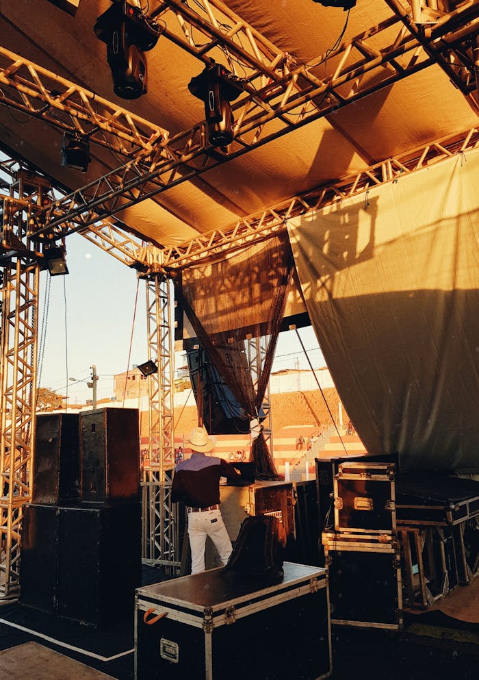 A man sets up equipment on stage with dramatic lighting at sunset.